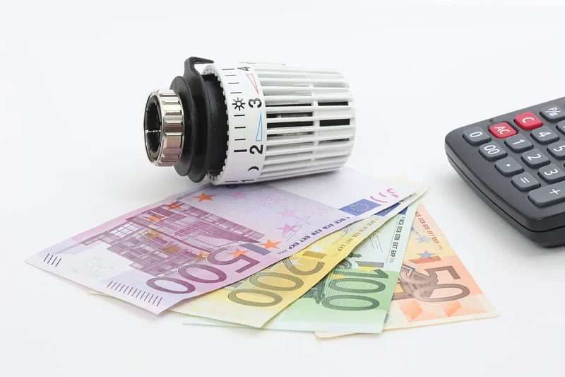 Głowica termostatyczna grzejnika leżąca na banknotach euro obok kalkulatora, symbol kosztów ogrzewania